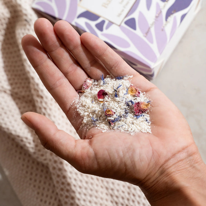 Hand holding a small amount of colorful dried flowers and herbs over a textured fabric background.