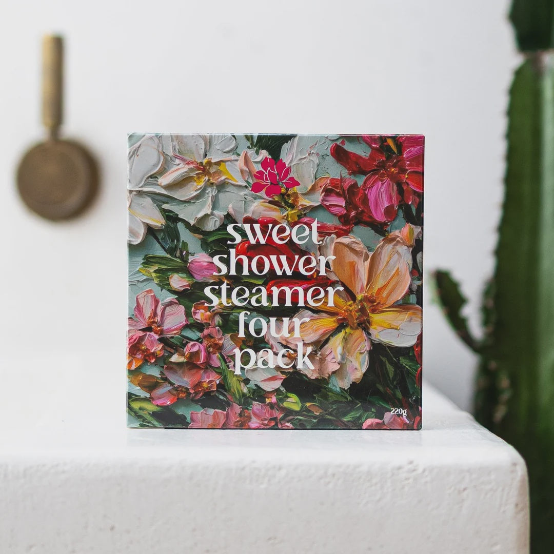 Floral packaging of a 'sweet shower steamer four pack' on a white surface with a cactus in the background.