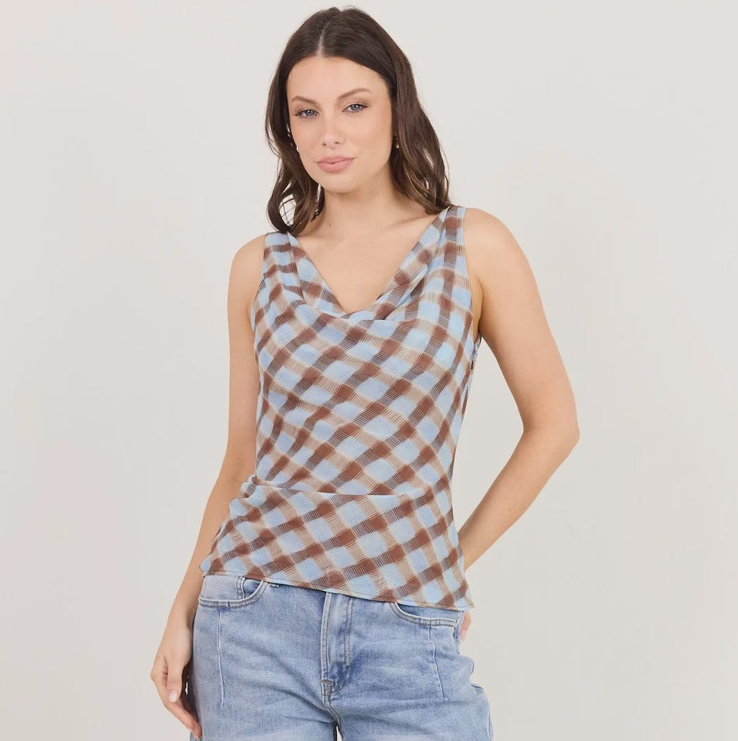 A woman modeling a sleeveless cowl-neck top with a brown and beige checkered pattern, paired with light-wash wide-leg jeans and black heeled sandals, against a plain off-white studio background.