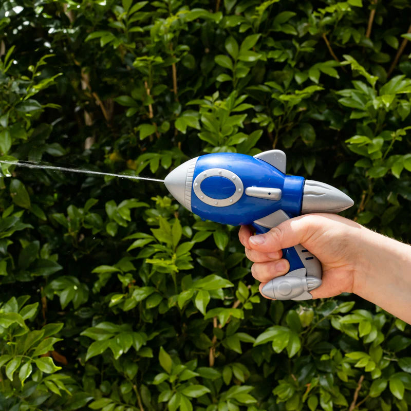 Hand holding a blue and gray toy rocket against a green hedge background