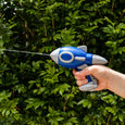 Hand holding a blue and gray toy rocket against a green hedge background