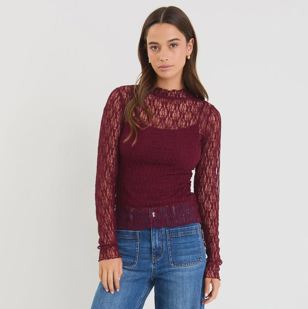 Woman wearing a burgundy lace top and blue jeans on a white background