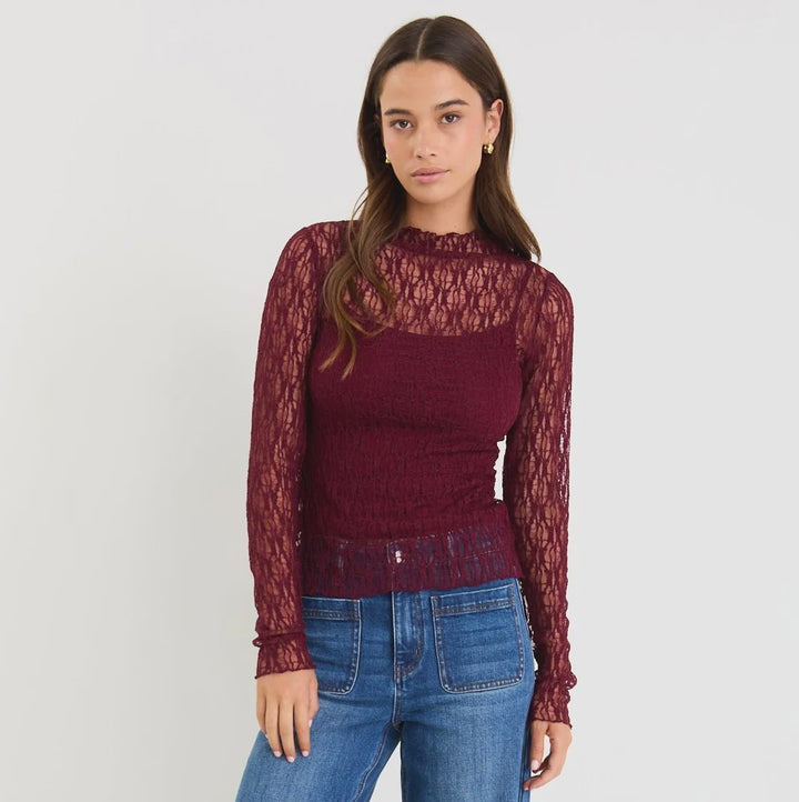 Woman wearing a burgundy lace top and blue jeans on a white background