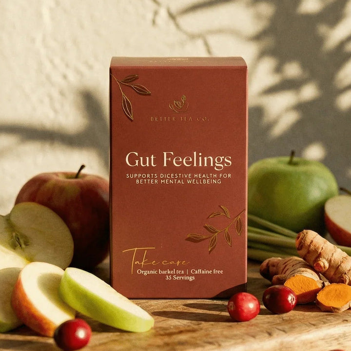 Box of 'Gut Feelings' supplement on a wooden board with apples, ginger, and berries.