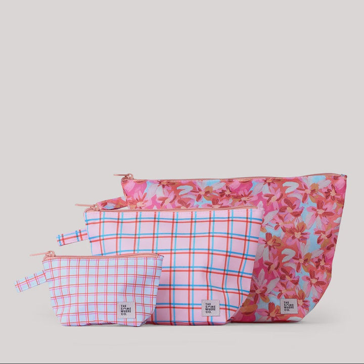 Three zippered pouches from The Happy Bag in pink and white plaid and floral print fabrics, arranged by size against a light gray background.