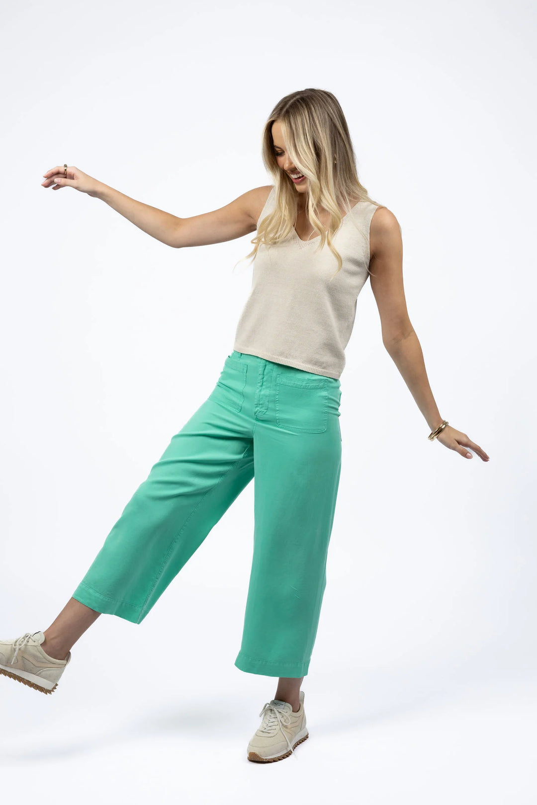 Woman wearing a beige sleeveless top and green pants on a white background