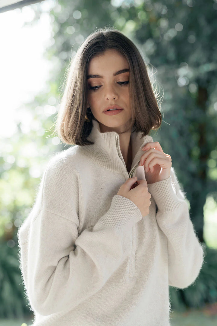 Woman wearing a white sweater with a blurred green background