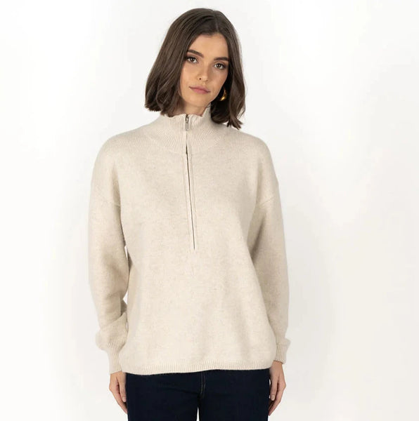 Person wearing a beige zip-up sweater and dark pants on a white background