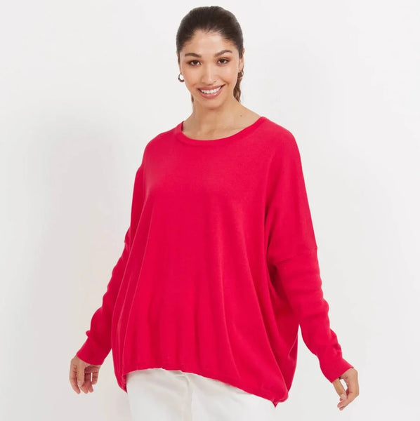Woman wearing a bright pink haven sweater and white pants on a white background