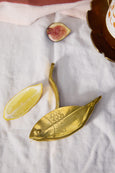 Gold fish-shaped object on a white fabric surface with a lemon wedge and fig slice.