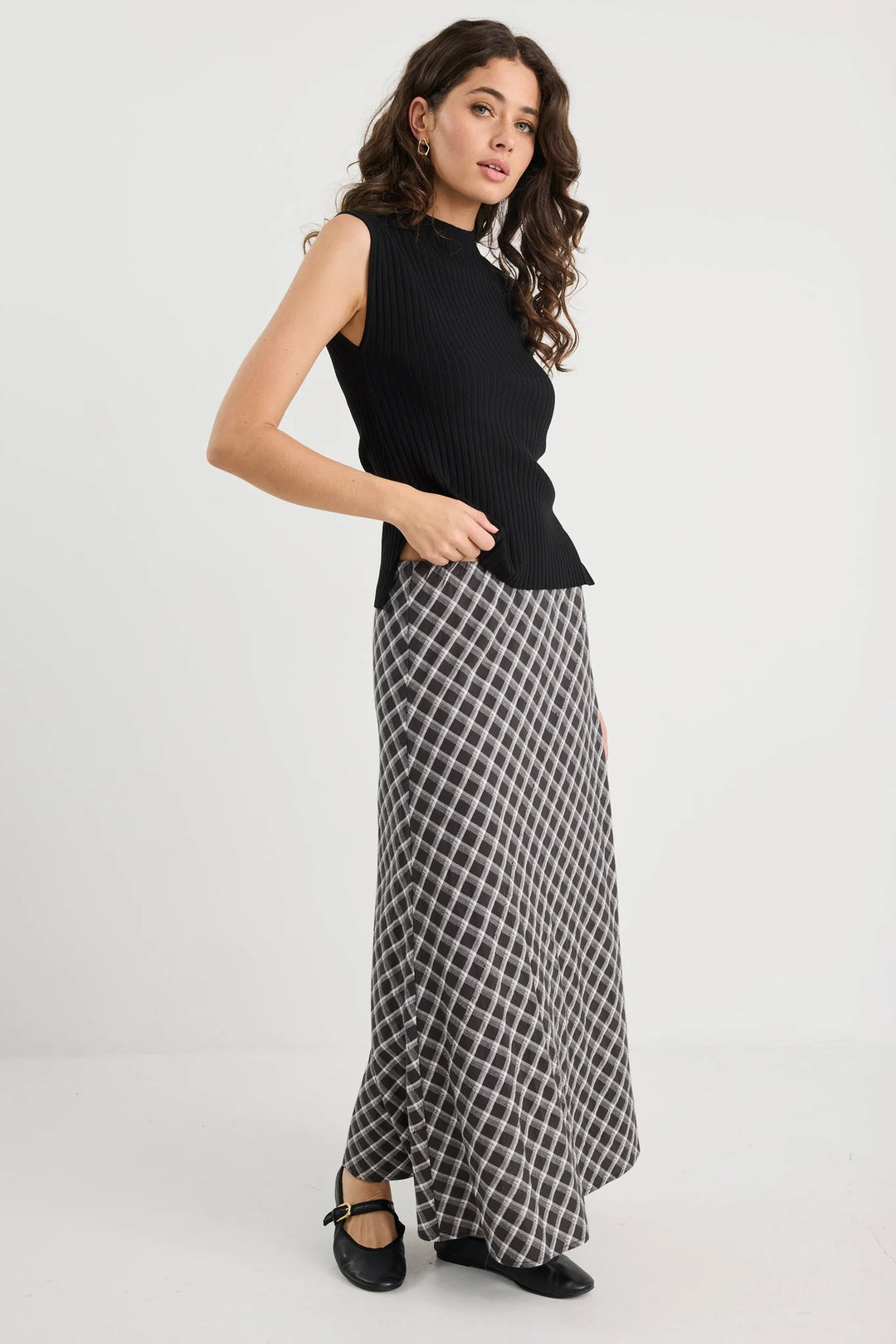 Woman wearing a black sleeveless top and plaid skirt on a white background