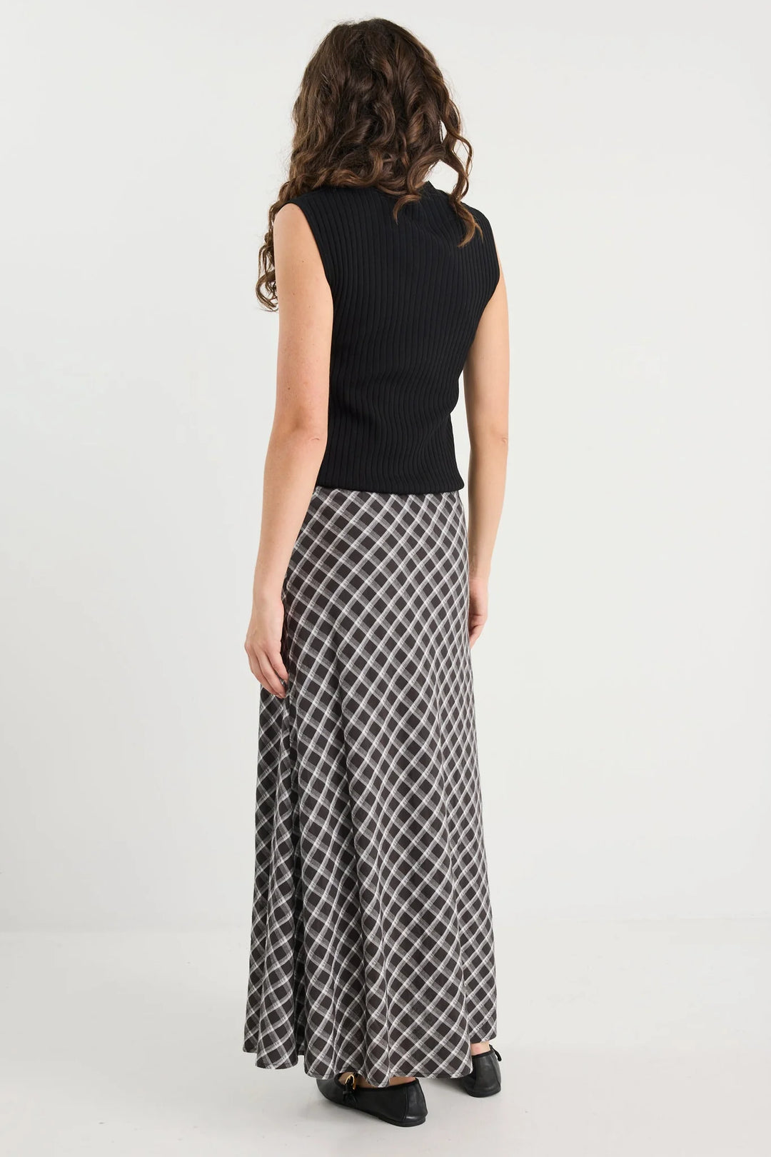 Woman wearing a black sleeveless top and plaid skirt on a white background