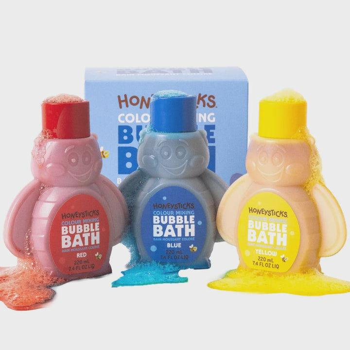 Three penguin-shaped bottles of Honysticks Colour Mixing Bubble Bath in red, blue, and yellow, arranged in front of a light blue product box on a white background.