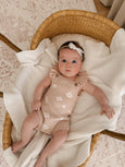 Baby in a floral romper lying in a wicker basket with white blanket