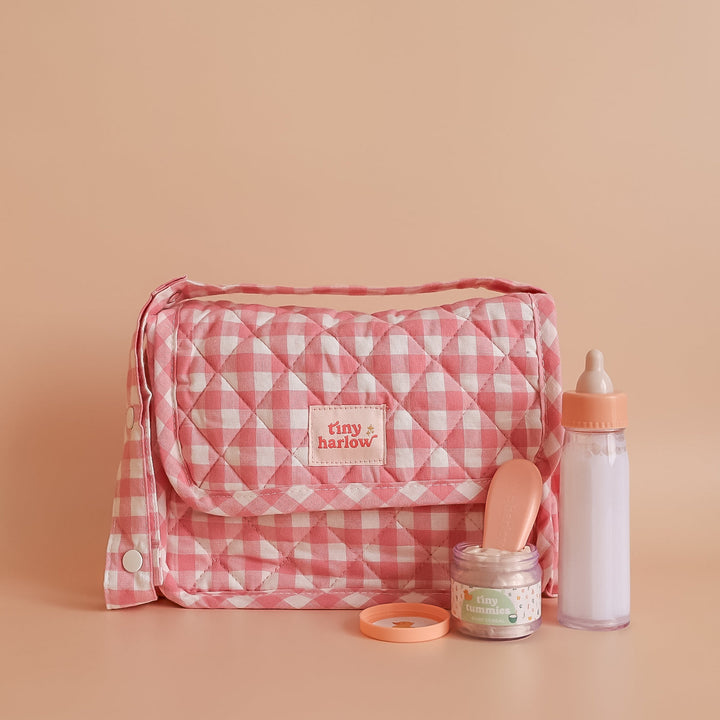 Tiny Harlow Pink checkered dolls bag with baby care items on a beige background
