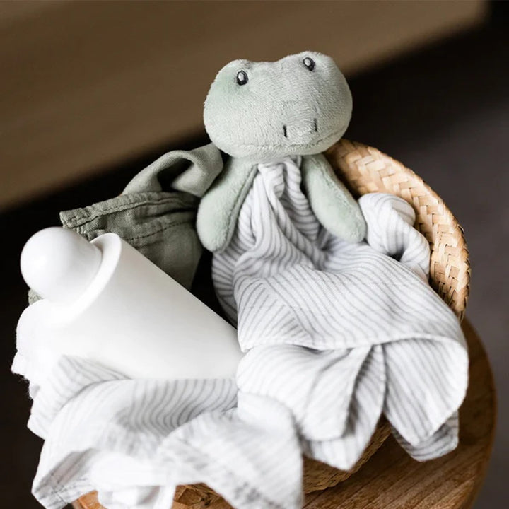 Stuffed toy frog with a blanket on a wooden surface