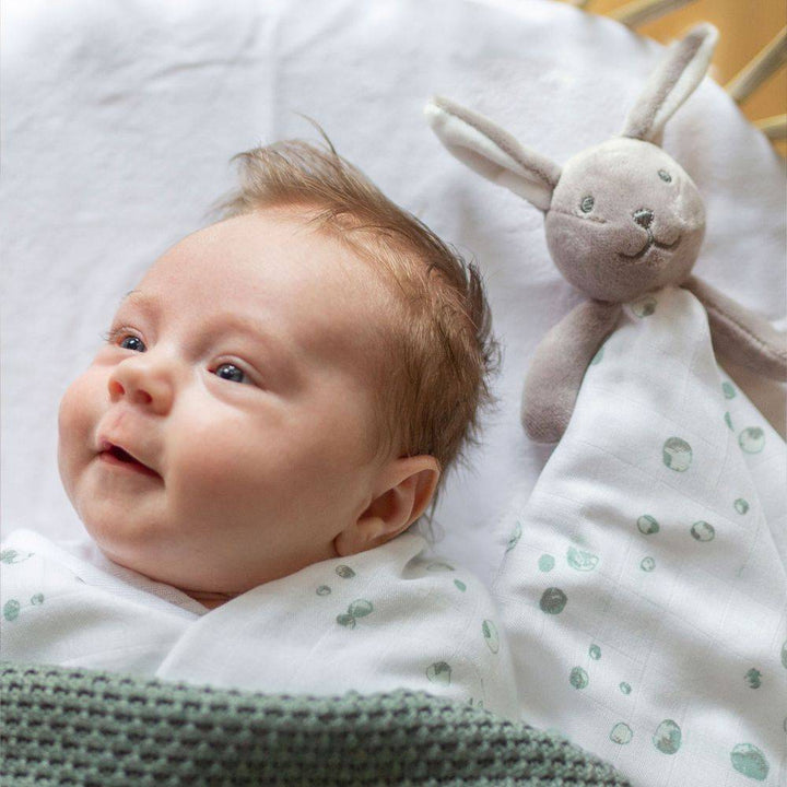 Baby lying on a white blanket with a soft toy next to it