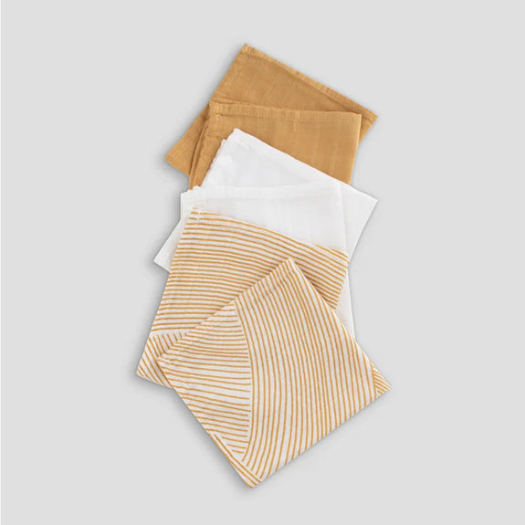 Set of muslin washcloths  in mustard yellow, white, and brown on a light gray background