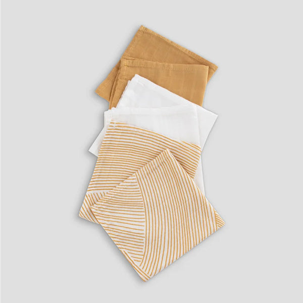 Set of muslin washcloths  in mustard yellow, white, and brown on a light gray background