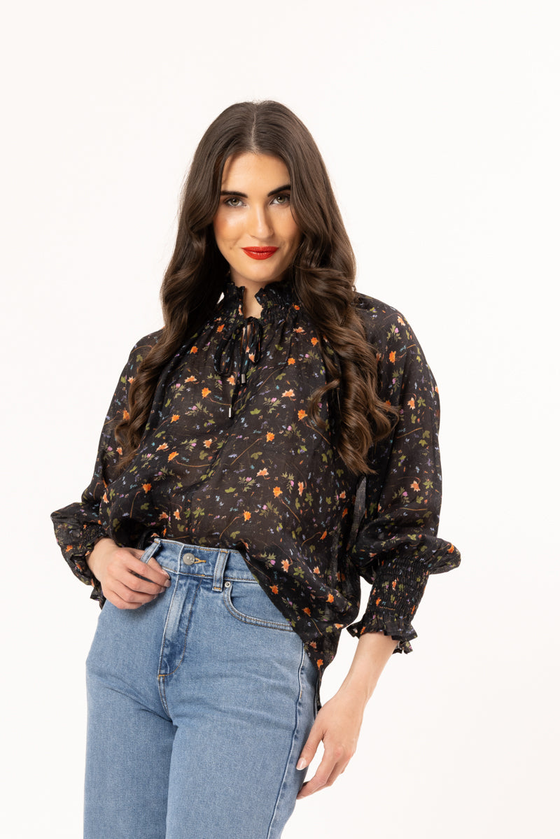 Woman wearing a black floral blouse and blue jeans on a white background
