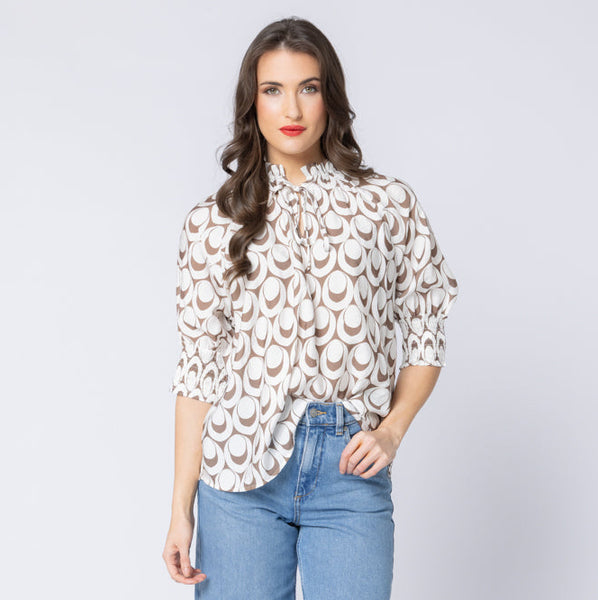 Woman wearing a patterned Leila & Luca blouse and blue jeans on a white background
