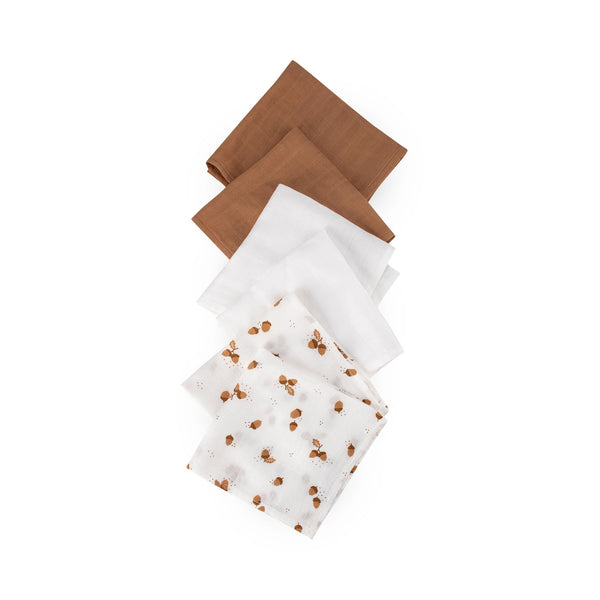 Three muslin fabric washcloths in brown, white, and white with brown pattern on a white background