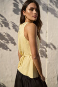 Woman wearing a yellow sleeveless top against a textured wall.