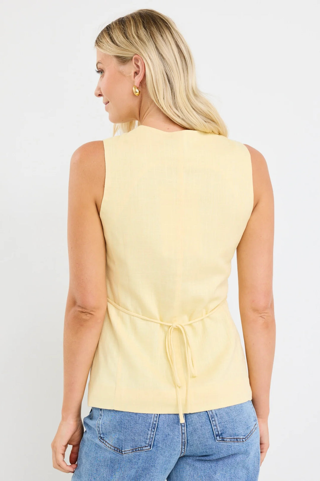 Woman wearing a yellow sleeveless top with a tie waist and blue jeans on a white background