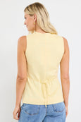 Woman wearing a yellow sleeveless top with a tie waist and blue jeans on a white background