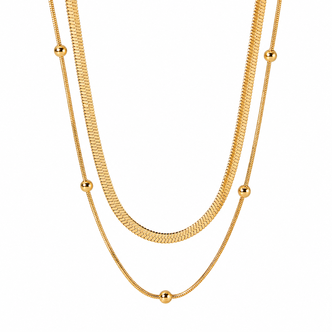 A gold-toned double-strand necklace featuring a textured snake chain and a finer chain with evenly spaced small spherical beads, displayed against a solid white background.