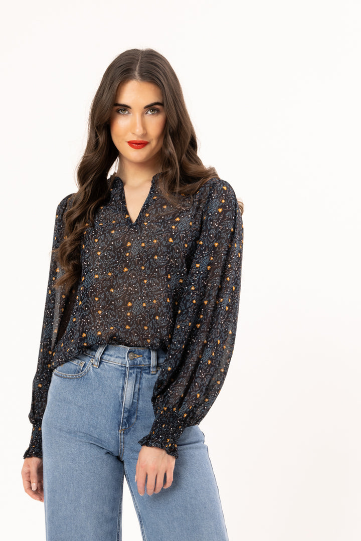 Woman wearing a patterned blouse and jeans on a white background