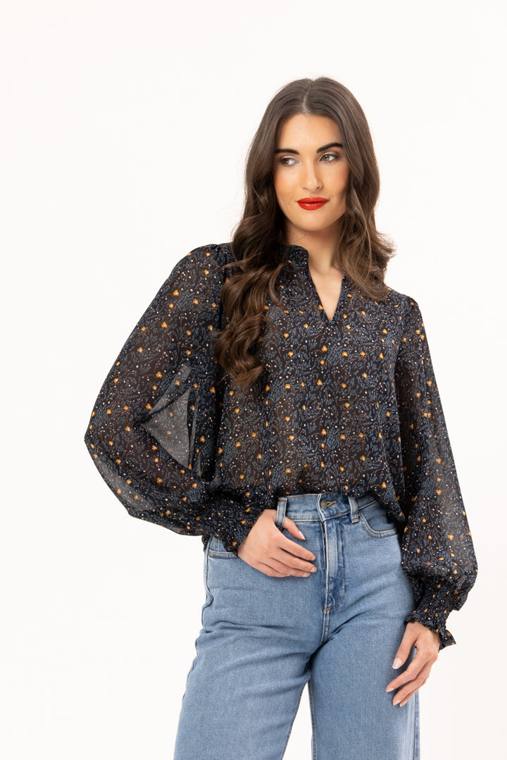 Woman wearing a black blouse with gold polka dots and blue jeans on a white background