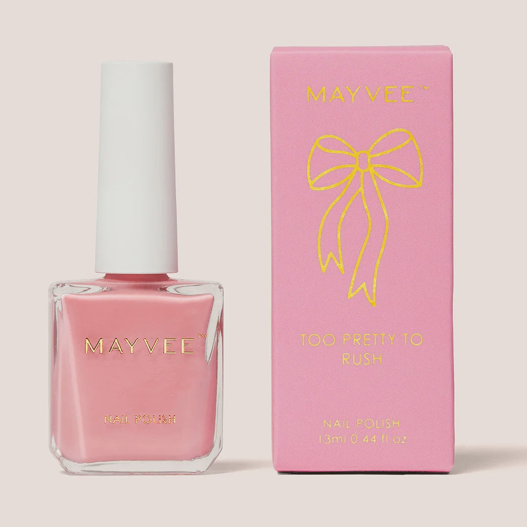 A bottle of MAYVEE nail polish in the shade 'Too Pretty to Blush' next to its pink packaging box with a gold bow graphic, set against a solid light beige background.
