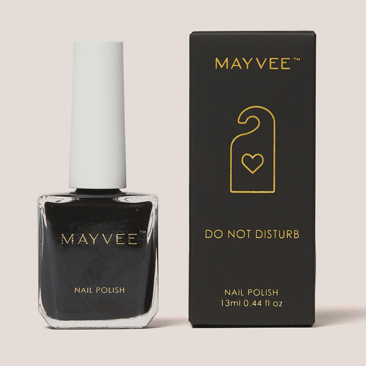 Mayvee nail polish bottle in a very dark black shade next to its black packaging box with gold lettering and a hangtag graphic, on a solid light beige background.
