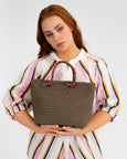 Woman holding a brown woven handbag against a plain background
