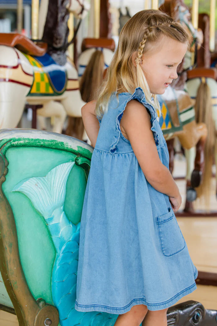 Young girl in a Milky blue dress standing on a carousel with colorful horses in the background