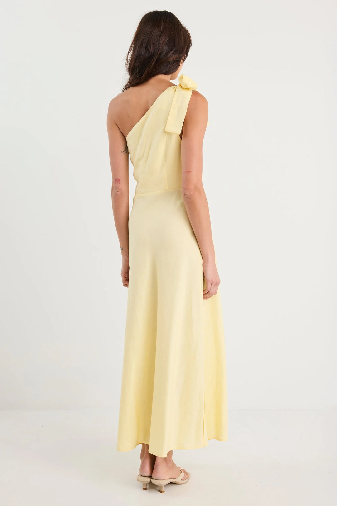 Woman wearing a light yellow one-shoulder dress on a white background