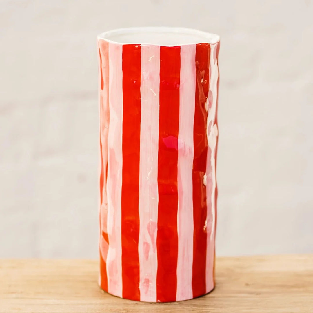 Red and white striped vase on a wooden surface with a light gray background