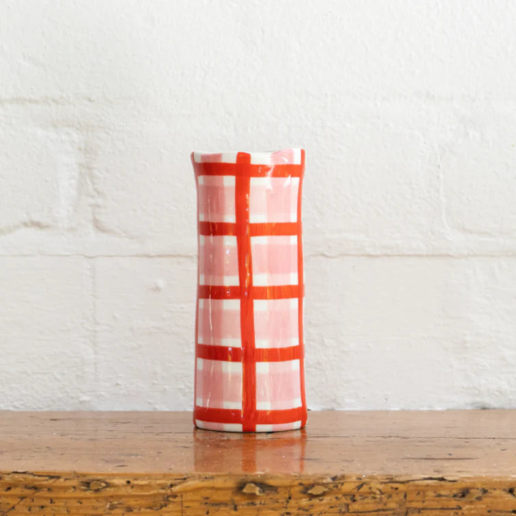 Red and white checkered vase on a wooden surface with a white brick wall background