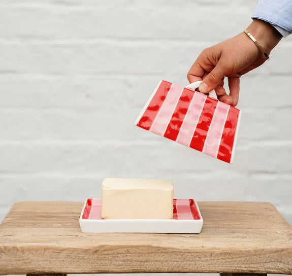 Hand holding a red and white striped soap dish with a bar of soap on a wooden surface.