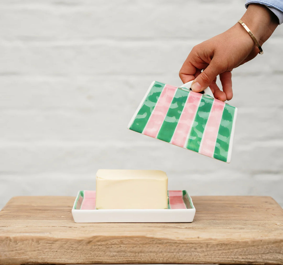 Hand holding a striped soap dish with a bar of soap on a wooden surface