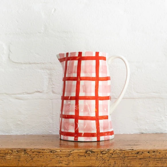 Ceramic pitcher with red and white checkered pattern on a wooden surface with a white textured wall background