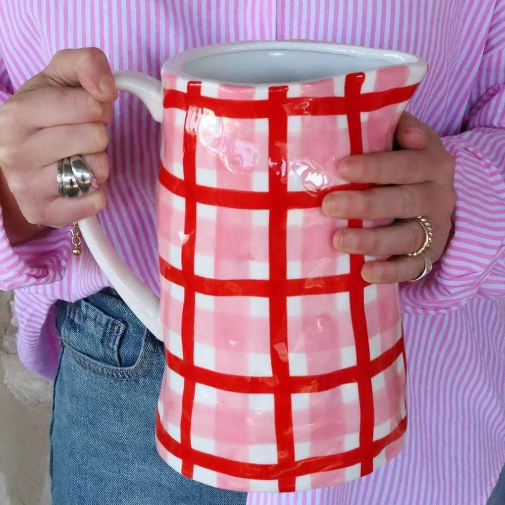 Person holding a red and white checkered mug with a pink shirt and jeans.