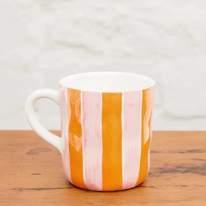 Mug with orange and pink vertical stripes on a wooden surface