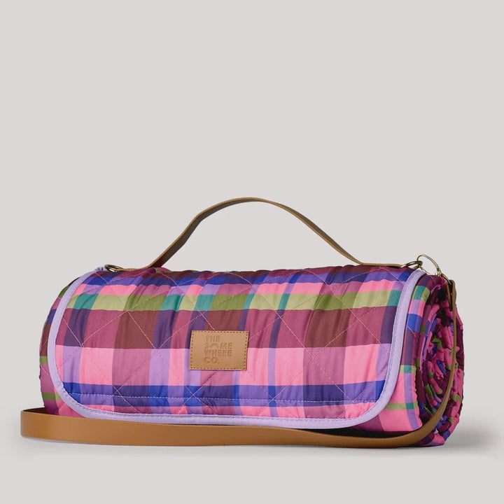 A quilted duffel bag with a vibrant pink, purple, and green plaid pattern, featuring a tan leather handle and strap, and a tan leather brand patch on the front.