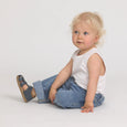 Child wearing a white sleeveless shirt and blue jeans sitting on a light gray background