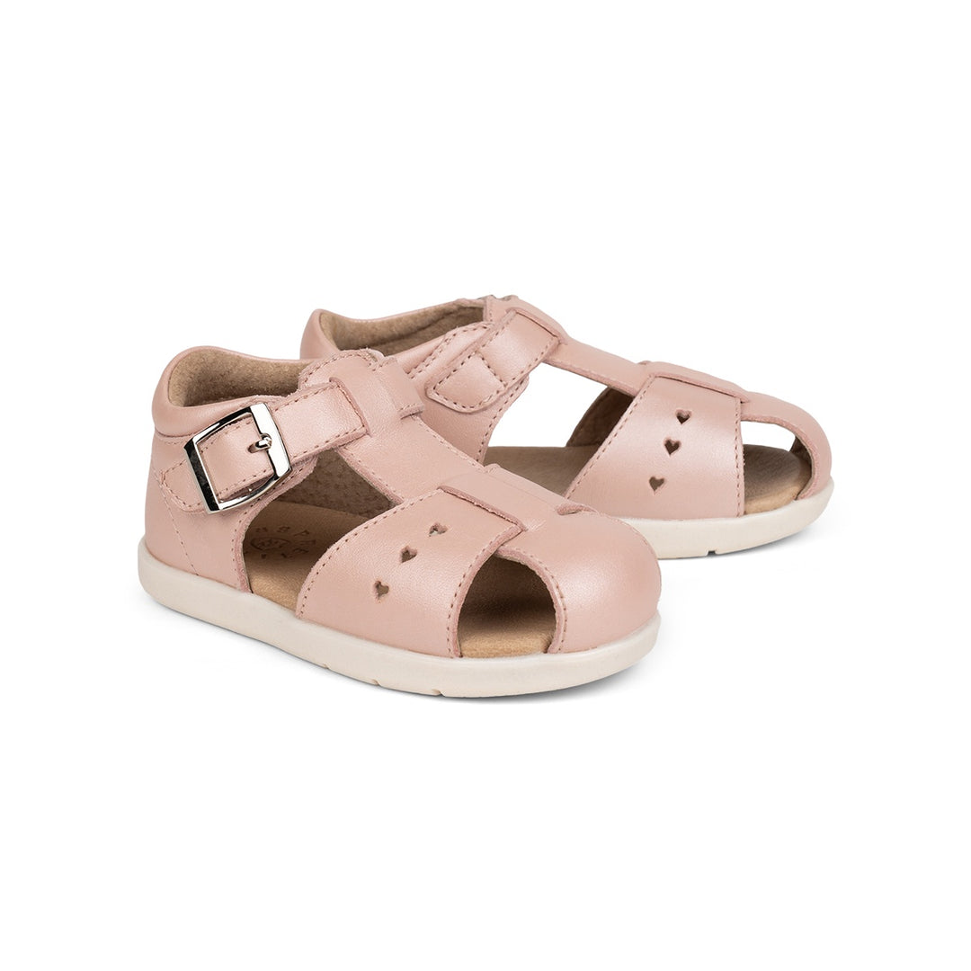 A pair of toddler sandals in light pink faux leather with heart-shaped cutouts, featuring adjustable straps with silver buckles and a cream-colored sole, shown on a white background.