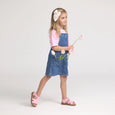 Young girl wearing a denim dress holding pink flowers on a white background