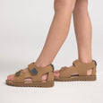 Tan Pretty Brave sandals worn by a person on a light gray background