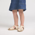 Person wearing beige pretty brave sandals and a blue denim skirt on a white background